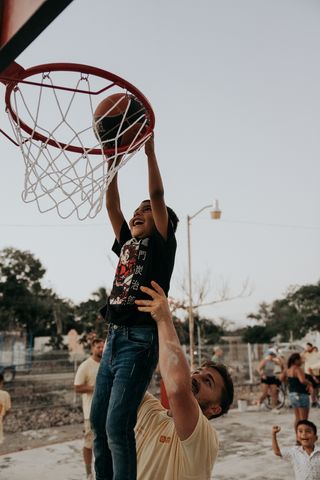 A man lifting a child to dunk a basketball